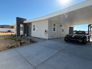 A modern house with a covered driveway, a black sports car, and a desert landscape. - 2-bedroom house in charming Joshua Tree with pool (Joshua Tree)