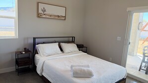 A bedroom with a bed, a nightstand, a bedside table, a framed picture on the wall, and a view through the door. - 2-bedroom house in charming Joshua Tree with pool (Joshua Tree)