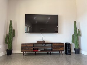 Un soggiorno con televisore a schermo piatto montato a parete, un mobile porta TV in legno e due cactus in vaso.