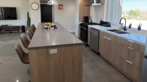 A modern kitchen with a central island, wooden cabinets, a built-in oven, and a window providing a view. - 2-bedroom house in charming Joshua Tree with pool (Joshua Tree)