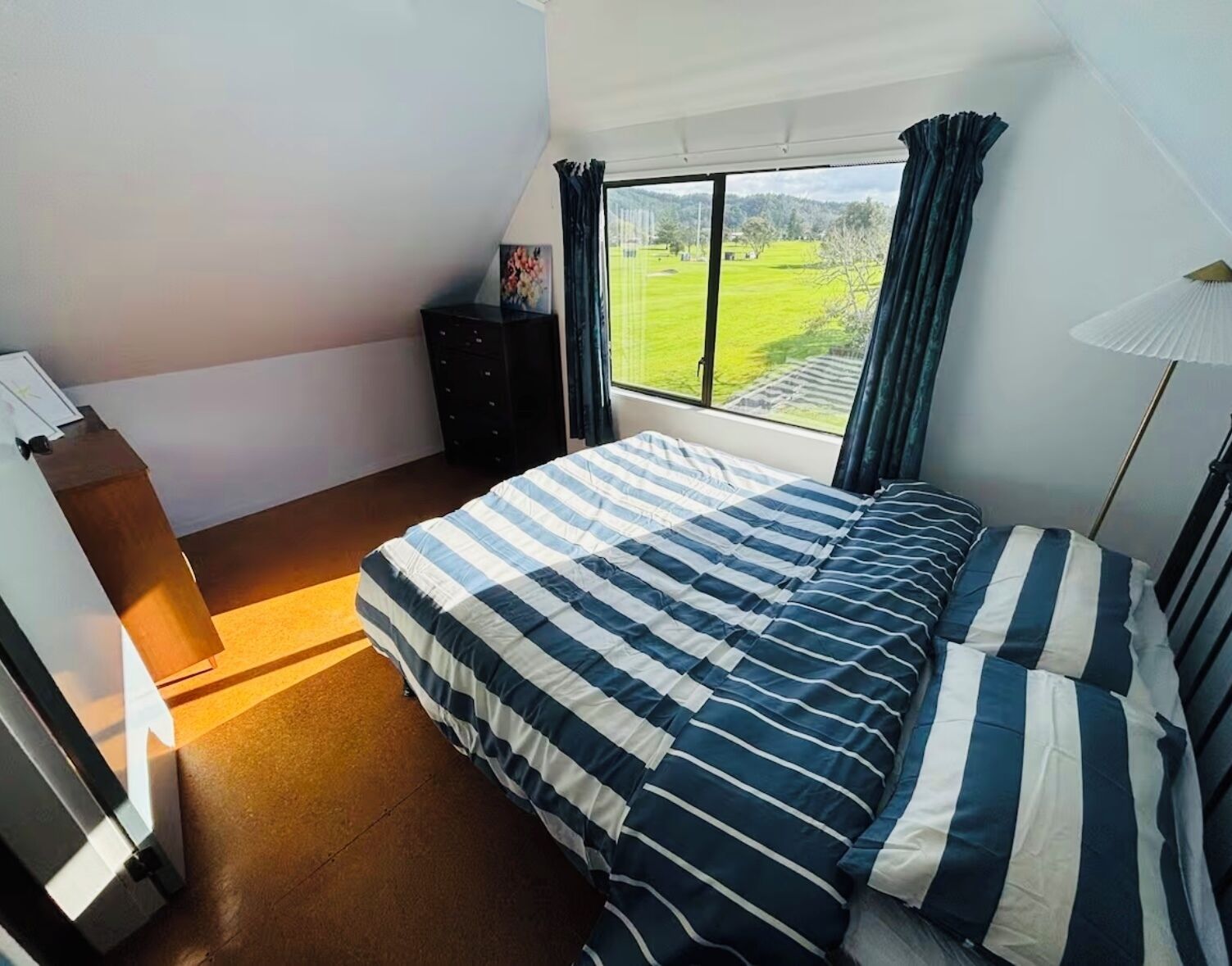 Une chambre à coucher avec un grand lit, une commode, un bureau et une fenêtre donnant sur un champ verdoyant.