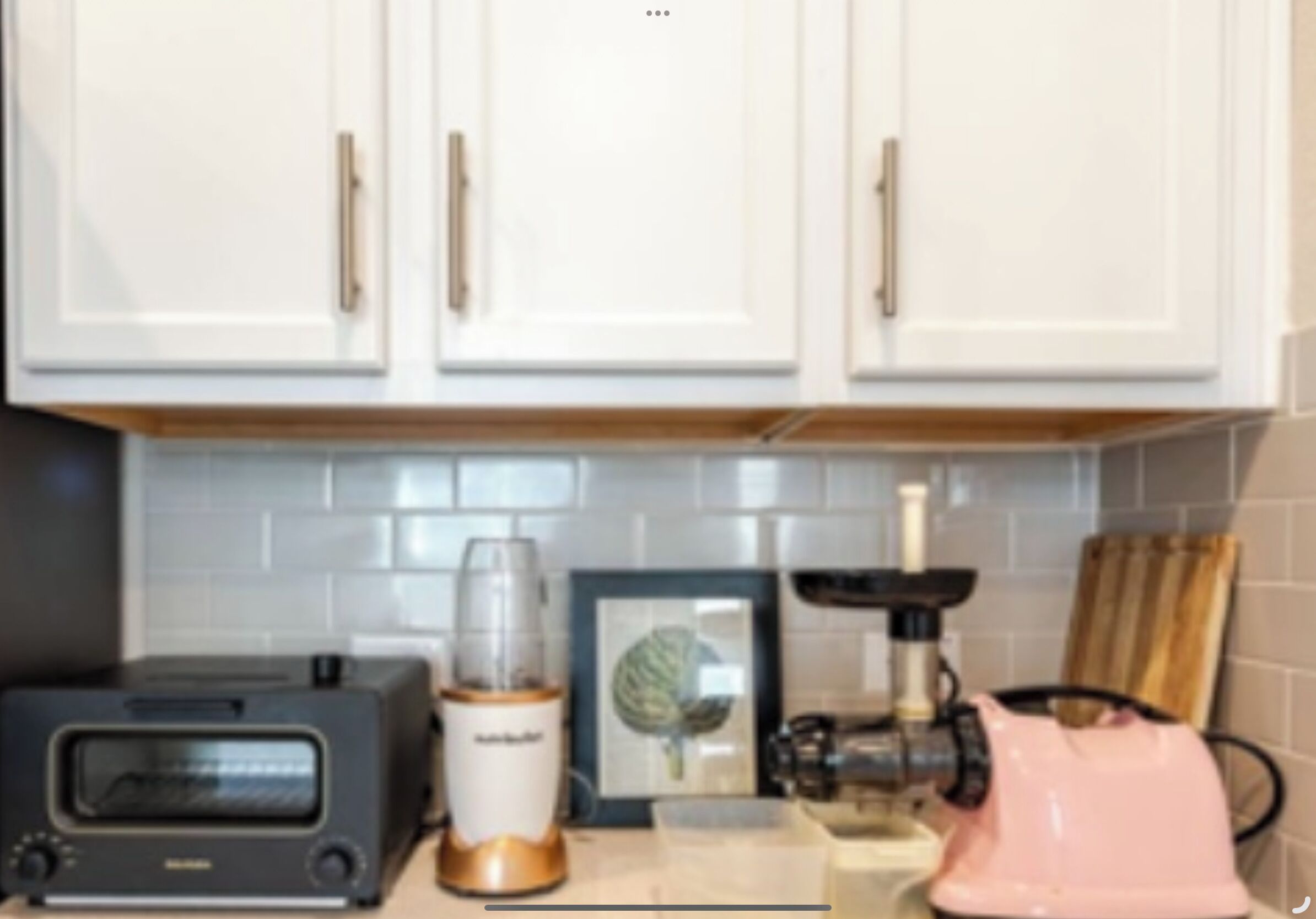 Una cocina con armarios blancos, un tostador, una licuadora y un electrodoméstico rosa.