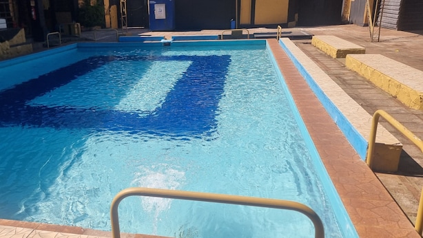 Ein Schwimmbecken mit klarem, blauem Wasser, einer gefliesten Liegefläche und einem Metallhandlauf.