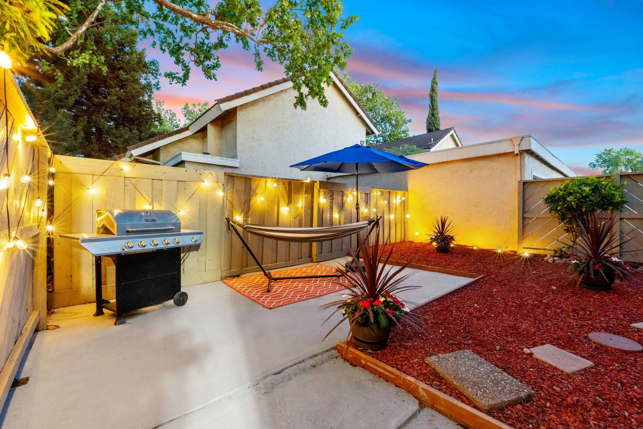 A backyard with a barbecue grill, a hammock, and string lights.