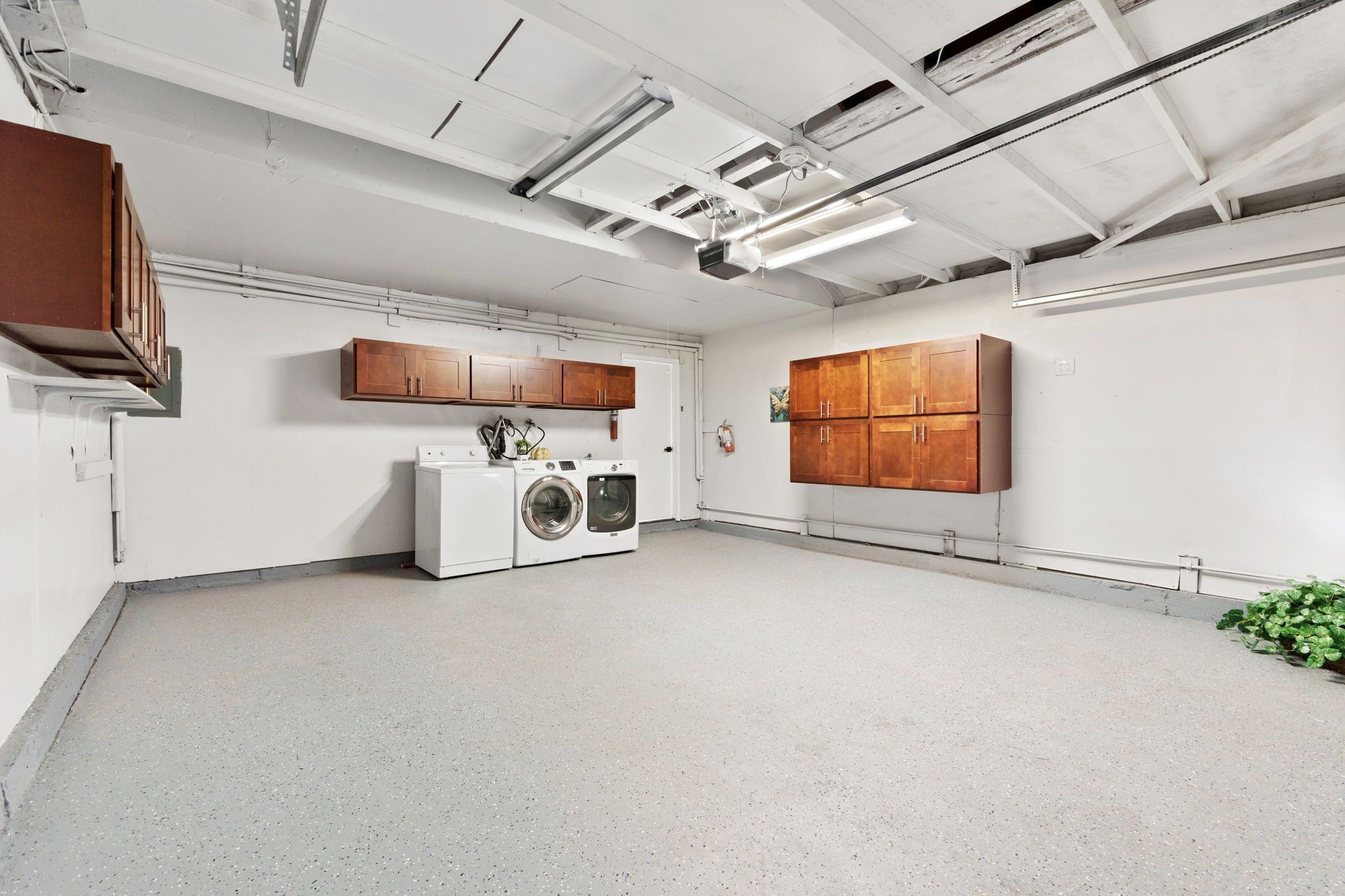 A laundry room with a washing machine, wooden cabinets, and a ceiling with exposed ductwork.
