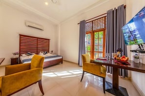 Una habitación de hotel con cama, una mesa de comedor con sillas, un televisor y un ventanal con cortinas.