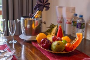 A fruit basket with various fruits, a silver pot with a bow, and a bottle of water on a table. - Owinmo Hotel & Reception Hall (Uluwitike, Galle)