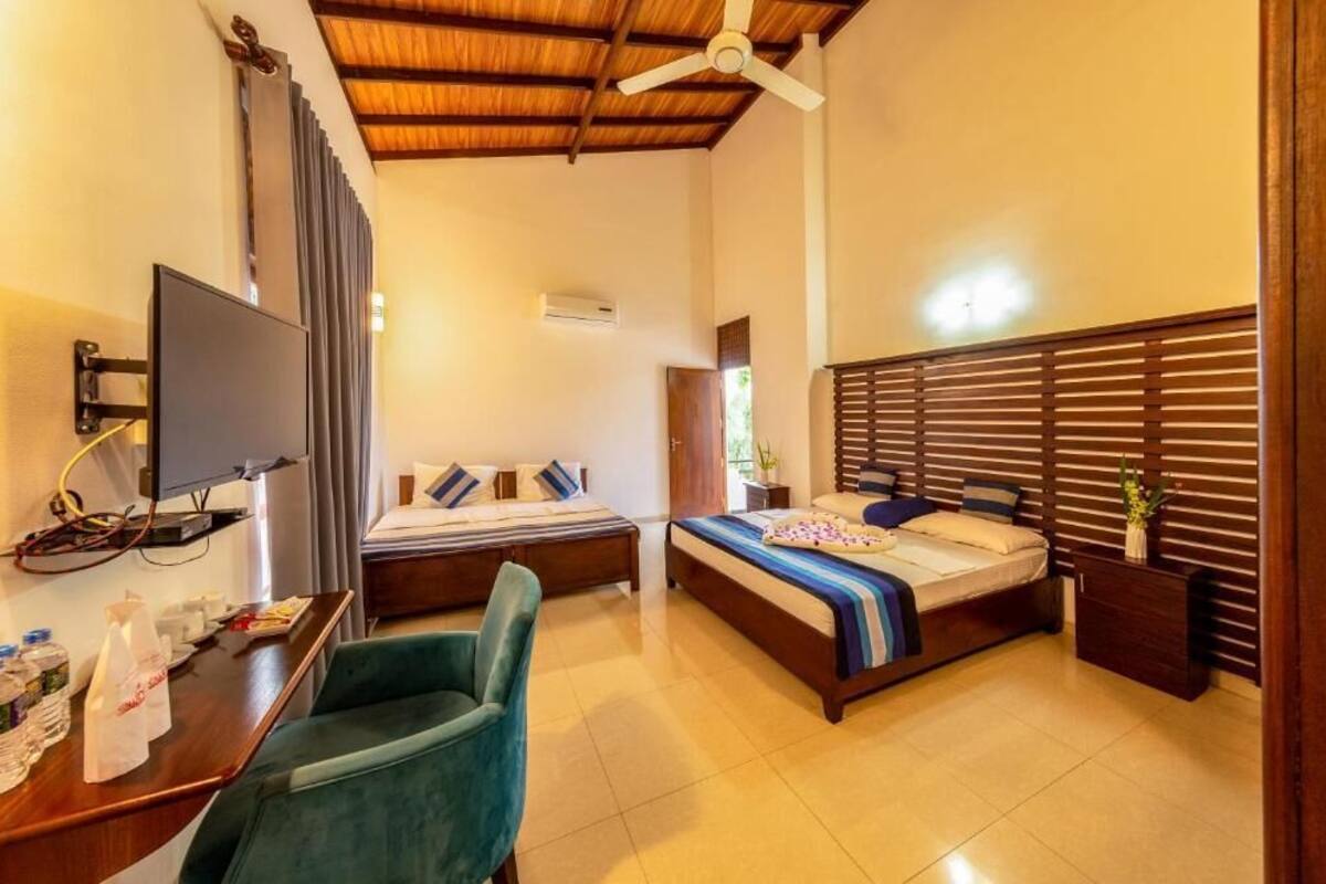 Une chambre d’hôtel avec deux lits, un bureau, une chaise, une télévision et un ventilateur de plafond.