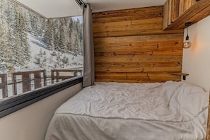Ein Schlafzimmer mit hölzernem Kopfteil, einem Fenster mit Blick auf schneebedeckte Bäume und einem Bett mit weißer Bettwäsche.