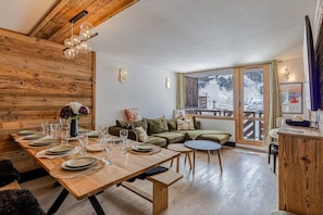 Ein Essbereich mit einem Holztisch, gedeckt für sechs Personen, einer Couch und Blick auf eine verschneite Landschaft durch große Fenster.