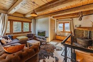 Ein gemütliches Cabin-Interieur mit einer Couch, Fernseher, Kamin und rustikalen Einrichtungsgegenständen.