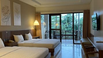 Habitación de hotel con dos camas, un escritorio, una silla, un televisor y un balcón con vistas a árboles.