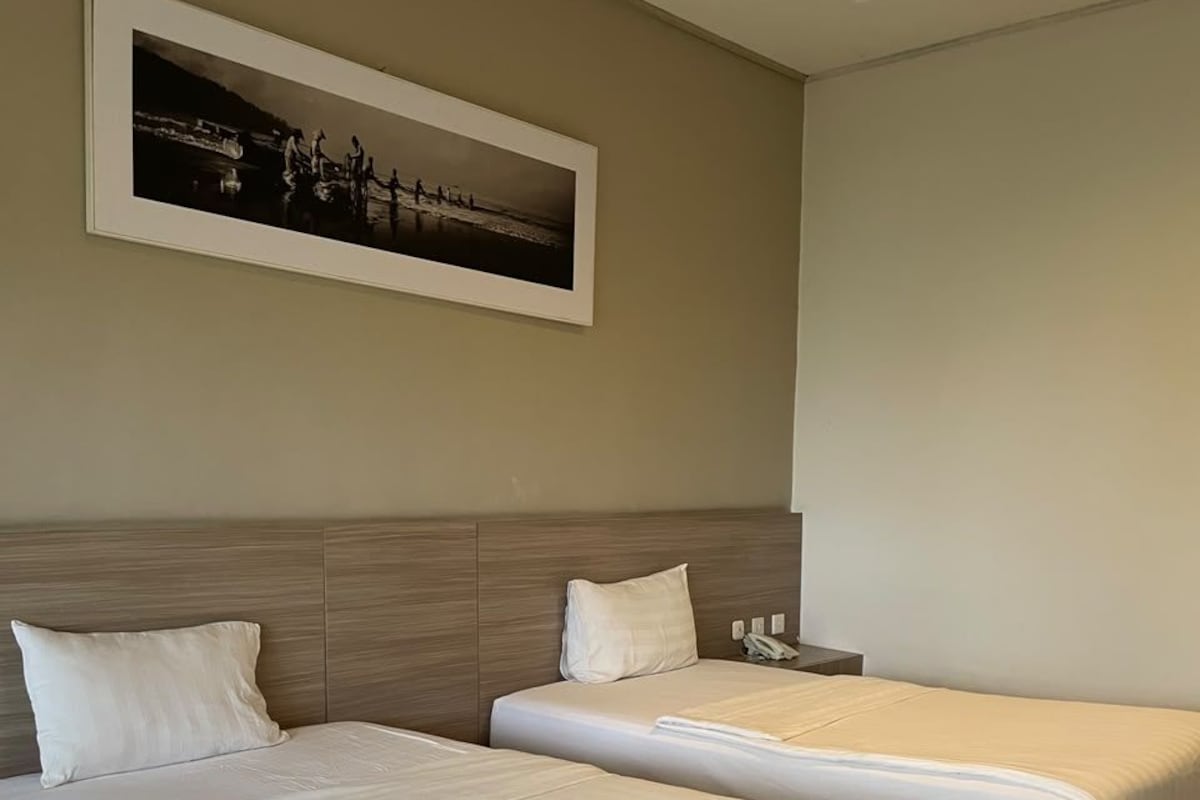 Habitación de hotel con dos camas, cabecero, mesita de noche con teléfono y un cuadro en la pared.