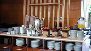 A buffet setup with stacked plates, a coffee machine, and a fruit bowl.