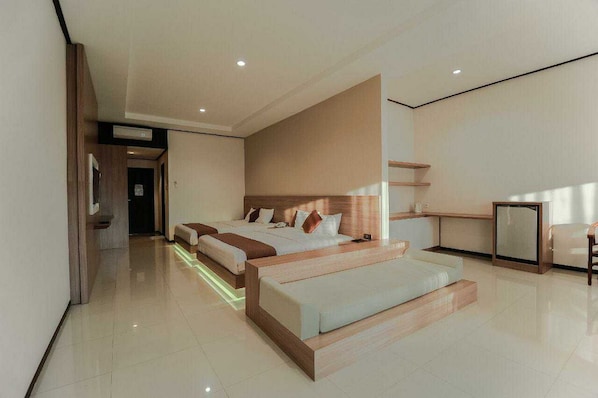 A modern hotel room with a large bed, a bedside table, a small desk, and a seating area.
