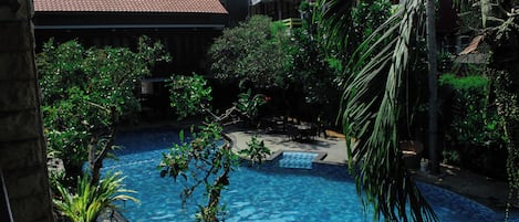 A swimming pool surrounded by lush greenery and buildings with red-tiled roofs.