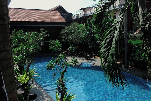 A swimming pool surrounded by lush greenery and buildings with red-tiled roofs.