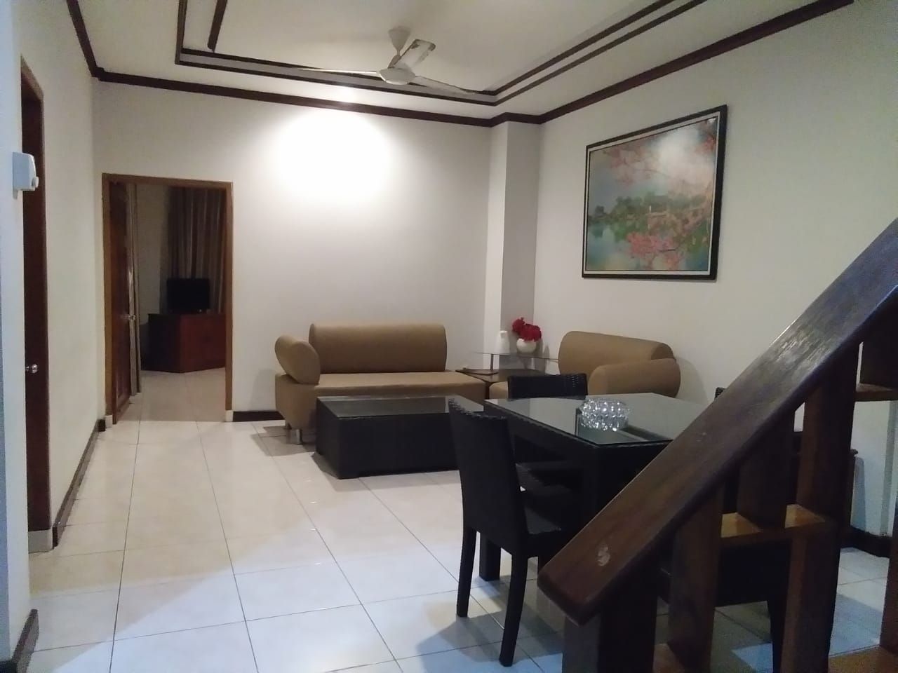 Una sala de estar con sofá, una mesa de centro y una mesa de comedor con sillas. Se ve una escalera en primer plano.