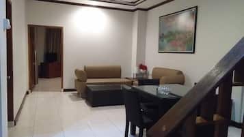 Una sala de estar con sofá, una mesa de centro y una mesa de comedor con sillas. Se ve una escalera en primer plano.