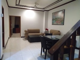 Una sala de estar con sofá, una mesa de centro y una mesa de comedor con sillas. Se ve una escalera en primer plano.