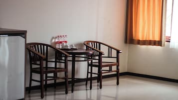 Un pequeño comedor con una mesa y dos sillas, un refrigerador y una ventana con cortinas.