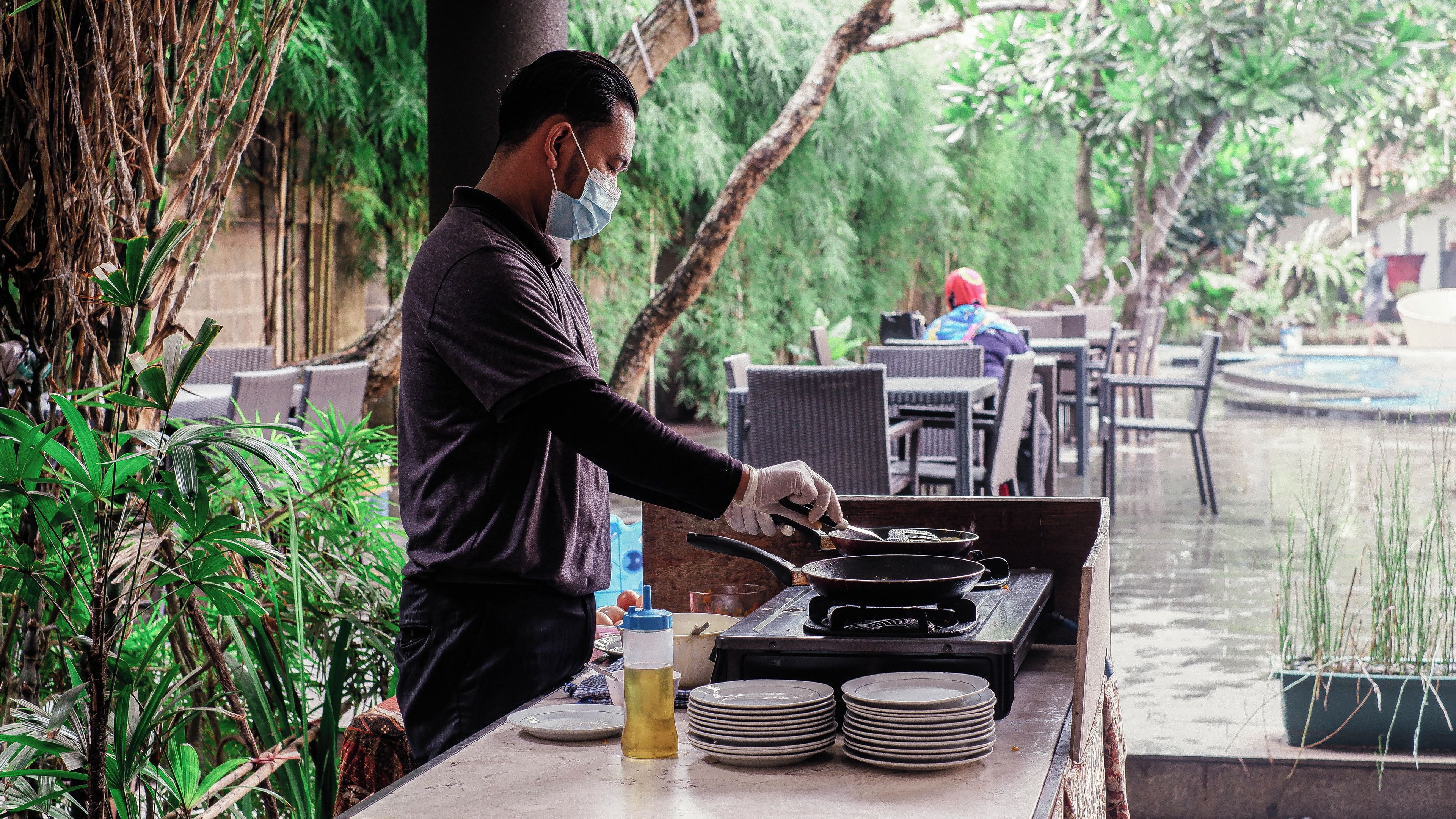 Una persona cocina al aire libre con una mesa, sillas y un elemento acuático al fondo.