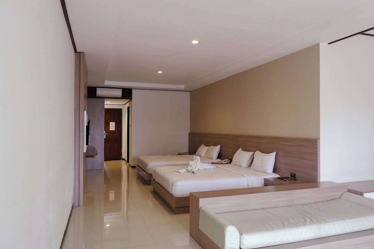 Habitación de hotel con dos camas, un sofá, un televisor de pantalla plana y un cabecero de madera.