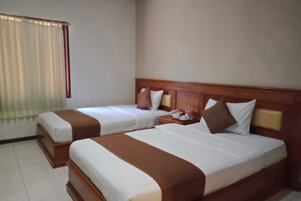 Una camera d'albergo con due letti, una testiera in legno, un comodino con una lampada e una finestra con tende.