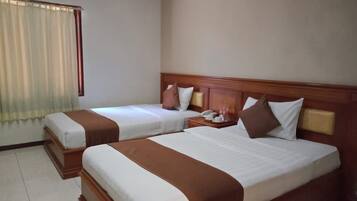 Habitación de hotel con dos camas, cabecera de madera, mesita de noche con lámpara y ventana con cortinas.