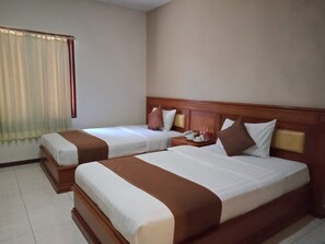 Habitación de hotel con dos camas, cabecera de madera, mesita de noche con lámpara y ventana con cortinas.