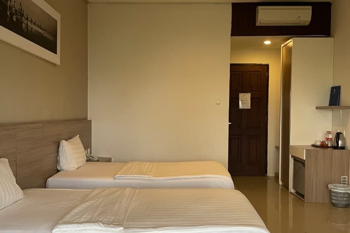Camera d'albergo con due letti, una testiera in legno, un tavolino con un bollitore e una porta che dà su un'altra stanza.