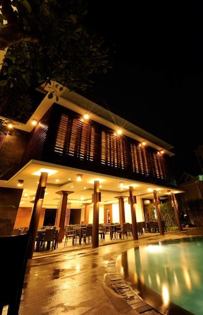 Un edificio moderno con piscina, mobiliario exterior y un patio cubierto.