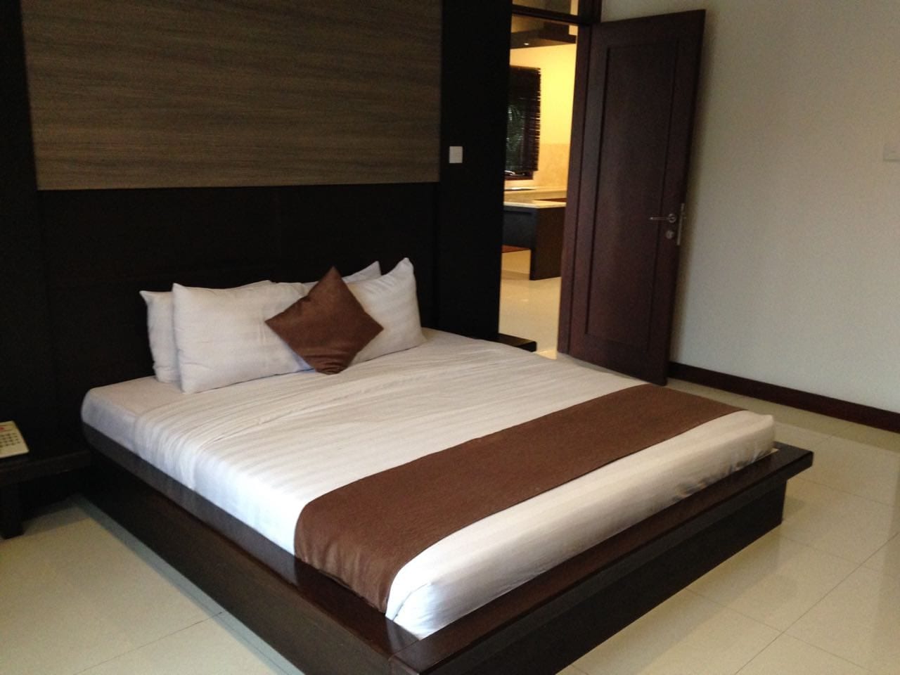 A modern hotel room with a large bed, a wooden headboard, and a dark brown accent wall.