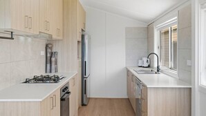 A compact kitchen with a gas stove, stainless steel refrigerator, and a dishwasher. - Central Coast Waterfront | 2BR + Jetty Access (Koolewong)