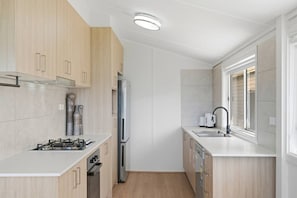 A compact kitchen with a gas stove, stainless steel refrigerator, and a dishwasher. - Central Coast Waterfront | 2BR + Jetty Access (Koolewong)