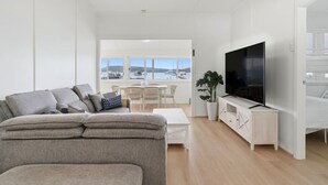 A modern living room with a sofa, TV, and a view of the sea. - Central Coast Waterfront | 2BR + Jetty Access (Koolewong)