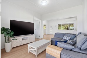 A modern living room with a flat-screen TV, a grey sofa, a white coffee table, and a potted plant.