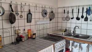 Et køkken med gasblus, ovn, vask og diverse køkkenredskaber hængende på væggen.