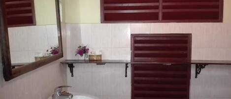 A bathroom with a white sink, a mirror, and two wooden window shutters.