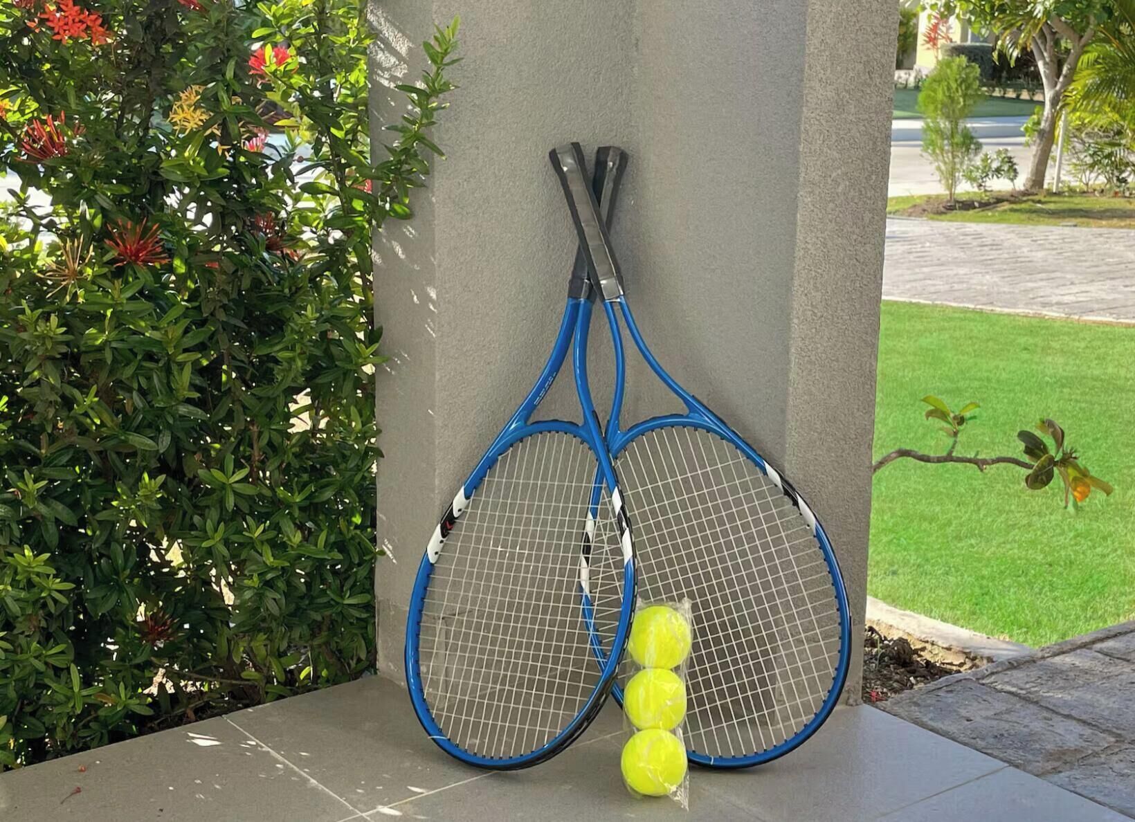 Two tennis rackets leaning against a wall with three tennis balls in front.