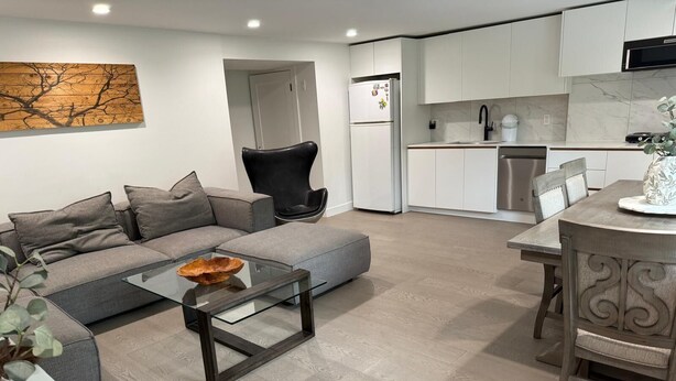 Een moderne woonkamer met een bank, een glazen salontafel en een eethoek met een tafel en stoelen.