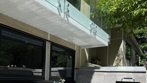 Een terras buiten met een tafel, stoelen, een barbecue en een glazen balustrade.