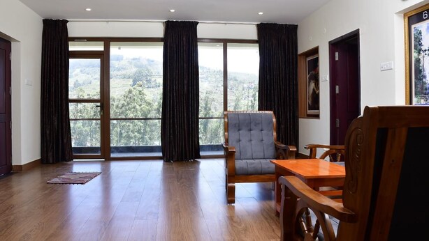 A spacious room with a large window, a wooden chair, a wooden table, and a door. - La Fiesta Resorts (Kodaikanal)