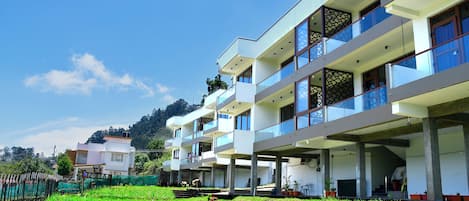 A multi-story building with balconies, a grassy area in front, and a clear sky.