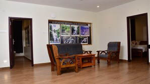 A room with wooden flooring, two wooden chairs, a small table, a bed with a white bedspread, and a wall with framed pictures of waterfalls. - La Fiesta Resorts (Kodaikanal)
