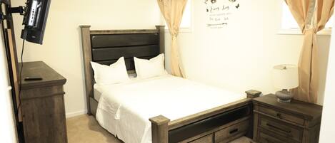 A bedroom with a bed, a nightstand, a dresser, a TV mounted on the wall, and a wall decoration.