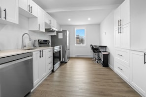 A modern kitchen with white cabinetry, stainless steel appliances, and a window providing natural light.