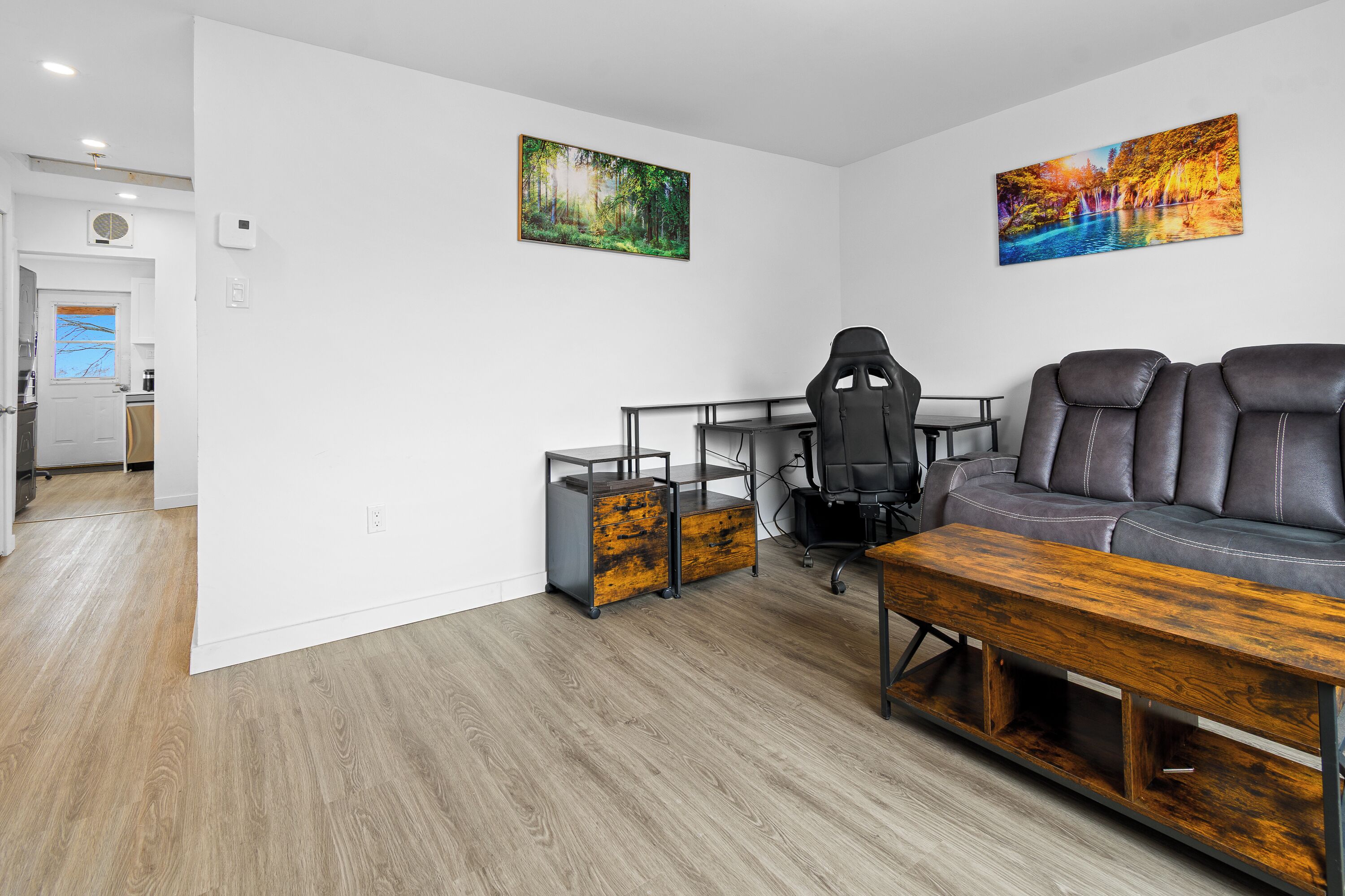 A modern living room with a sofa, gaming chair, wooden coffee table, and two wall-mounted paintings.
