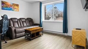 Una sala de estar con un sofá, una mesa de centro, un televisor y un ventanal con cortinas.