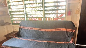 A sofa with a patterned cover, a window with a metal grid, and a fire extinguisher on the wall. - Charming beachfront studio cabana in sunny Placencia (Placencia)